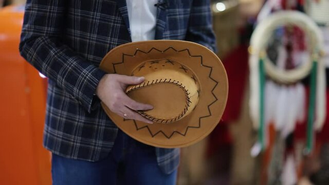 The male hand is holding a cowboy hat in hats store. Close up of handmade cowboy hat in shop of the Texas