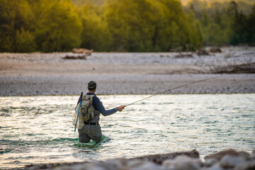 A fly fisherman casts his line while wading in the middle of a river