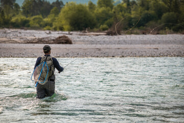 Close up of a fly fisherman casts his line while wading in the middle of a river