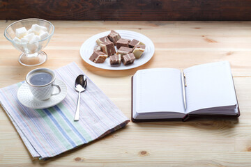 Cup of coffee on a wooden table with sweets and notepad.