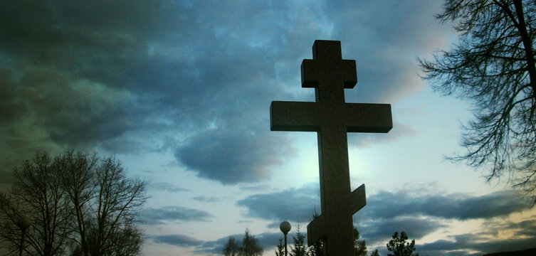 Cross in cemetry in evening under stormy sky. Life and death concept
