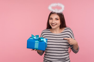 Portrait of happy angelic girl with saint halo over head pointing birthday gift and smiling,...