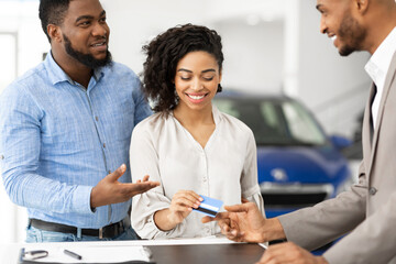 Couple Buying Car Giving Credit Card To Salesman In Dealership