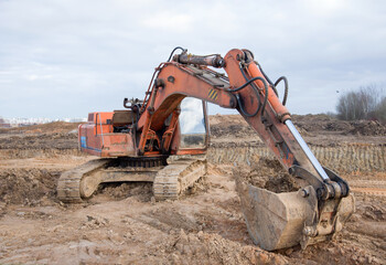 Fototapeta na wymiar Red excavator during earthworks at construction site. Backhoe digging the ground for the foundation and for laying sewer pipes district heating. Earth-moving heavy equipment