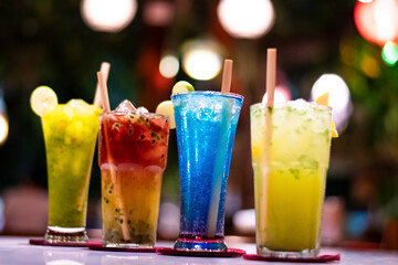 Cold multicolour alcoholic beverages in a fine dine restaurant garnished with lemon piece and ecofriendly wooden straw with bokeh