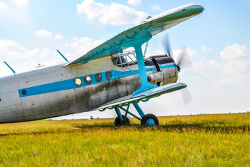 Small old private plane standing in spring fields by blue sky