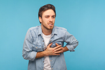 Cardiac problems. Portrait of stressed out, worried man in denim shirt clutching chest, suffering...