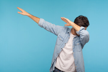 Dab dance. Portrait of man in denim shirt making dabbing movement, famous internet meme of success victory, expressing happiness and following trends. indoor studio shot isolated on blue background