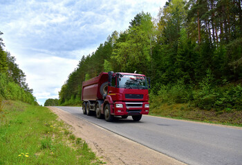 Obraz premium Tipper Dump Truck transported sand from the quarry on driving along highway. Modern Heavy Duty Dump Truck with unloads goods by itself through hydraulic or mechanical lifting