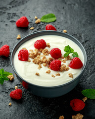 Greek yogurt with granola and raspberry in black bowl. Healthy breakfast food or snack