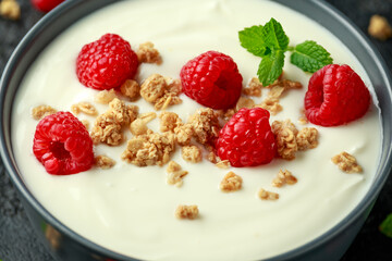 Greek yogurt with granola and raspberry in black bowl. Healthy breakfast food or snack