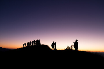 Fototapeta na wymiar Silhouette of group people standing on the mountain and look to the forward at twilight time.