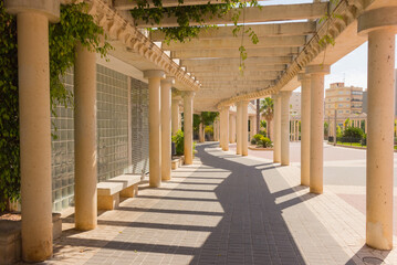 Fototapeta na wymiar Long empty corridor with arch and stone columns in the park, old town, Calpe, Spain