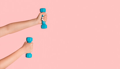Cropped view of young girl lifting dumbbells on pink background, copy space
