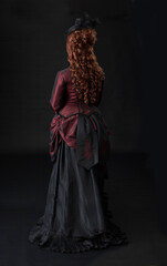 Fototapeta na wymiar A young Victorian woman in a dark red and black ensemble against a black backdrop