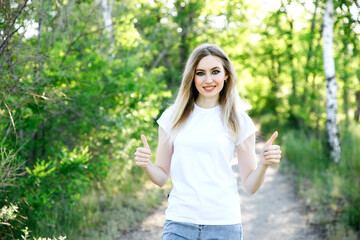 woman in a white t-shirt showing thumbs up on a background of green trees. mockup.