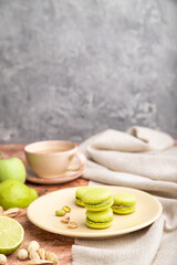 Green macarons or macaroons cakes with cup of coffee on a brown and gray concrete background. Side view, selective focus, copy space.