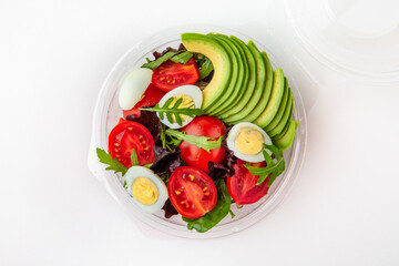 Salad in plastic package for take away or food delivery isolated on a white background. Nutritional Diet Snack with tomatoes, avocado, quail egg.