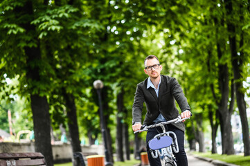 Use environmentally friendly modes of transport. Handsome young man in smart casual wear and eyeglasses is riding a bike to the office