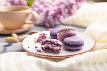 Fototapeta na wymiar Purple macarons or macaroons cakes with cup of coffee on a gray wooden background. Side view, selective focus.