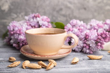 Cup of coffee with lilac and almonds on a gray wooden background. Side view.
