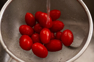 Colorful red cherry tomatoes washed in a stainless colander, on round silver sink background, copy space