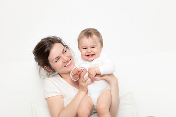Happy mother playing with baby on white sofa