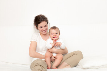 Fototapeta na wymiar Happy mother playing with baby on white sofa