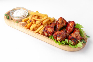 Grilled chicken wings with sauce and french fries on a wooden stand. Banquet festive dishes. Gourmet restaurant menu. White background.
