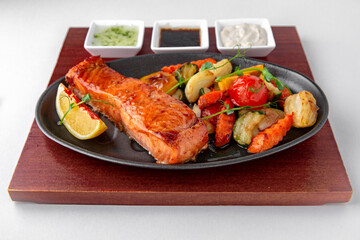 Grilled salmon fillet with vegetables and sauces on a wooden stand. Banquet festive dishes. Gourmet restaurant menu. White background.