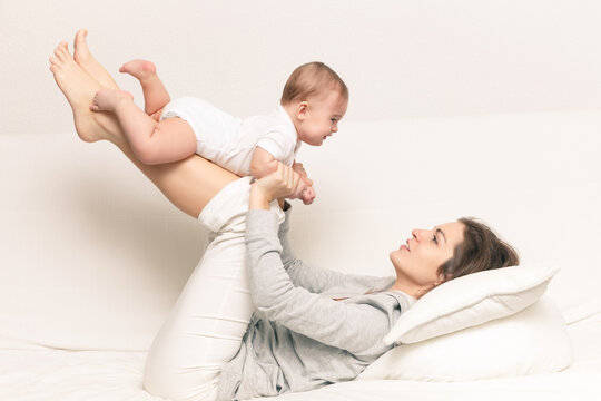 Happy mother playing with baby on white sofa