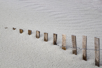 storm fence disappears into drifting beach sand dune