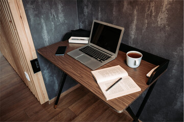 Modern wooden workplace with a notebook, tea, pen, diary and a mobile phone. Grey wall