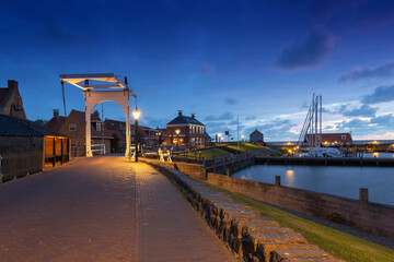 Fototapeta na wymiar Netherlands - Hindeloopen - a magical evening view of a stone path that leads over a drawbridge to the harbor, where boats are moored. Illuminated by evening lamps with a beautiful dark sky