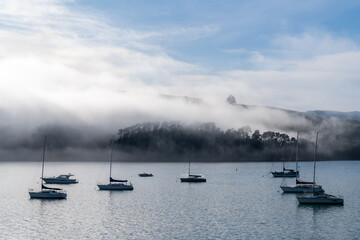 Fototapeta na wymiar Blue sky, white clouds, mist & aquamarine seas at Akaroa Harbor. Anchored are fishing boats & sailboats, along the Port at Akaroa, Canterbury, New Zealand.