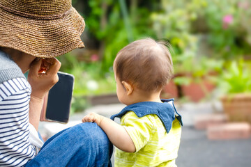 お庭でスマホを見ているおばあちゃんと孫の男の子