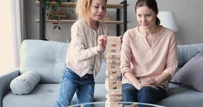 Overjoyed young mother celebrating win when little preschool redhead daughter ruined wooden tower. Small 7 years old adorable child girl failed in board game, having fun with mum indoors.