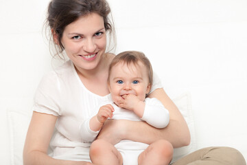 Fototapeta na wymiar Happy mother playing with baby on white sofa