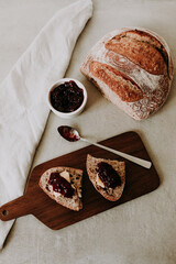 One slices of homemade sourdough bread with butter and raspberry jam on a wooden board – artisan bakery breakfast flat lay