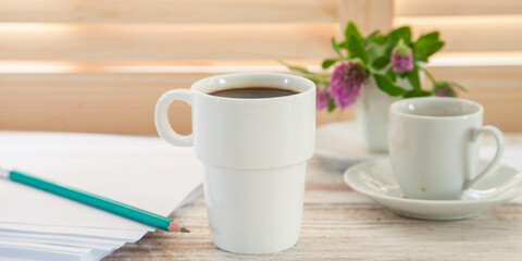 Office workplace with  coffee cup on wooden desk table in front of window with blinds, selective focus