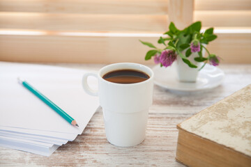 Office workplace with  coffee cup on wooden desk table in front of window with blinds, selective focus