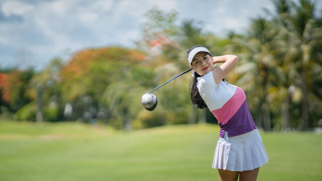 Asian female golfer swinging club on golf course green with copy space.