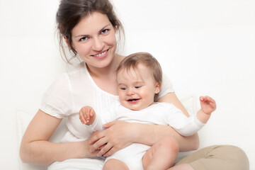 Obraz na płótnie Canvas Happy mother playing with baby on white sofa