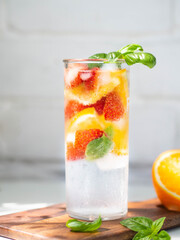 Fresh Summer Homemade lemonade with orange slices, strawbereies, basil and ice in glass on a white table.