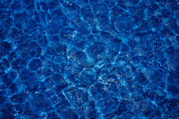 Swimming pool, blue clear water in the outdoor pool, with sun flare on the surface. Background of blue water in the pool