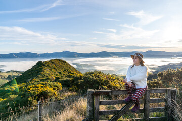 Naklejka na ściany i meble Happy carefree asian woman enjoying nature with layers of mountains and the mist in the morning at The peak of Bank Peninsula, Akaroa, New Zealand.