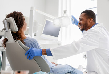 Obraz premium Cheerful male dentist talking to woman sitting in dentist chair