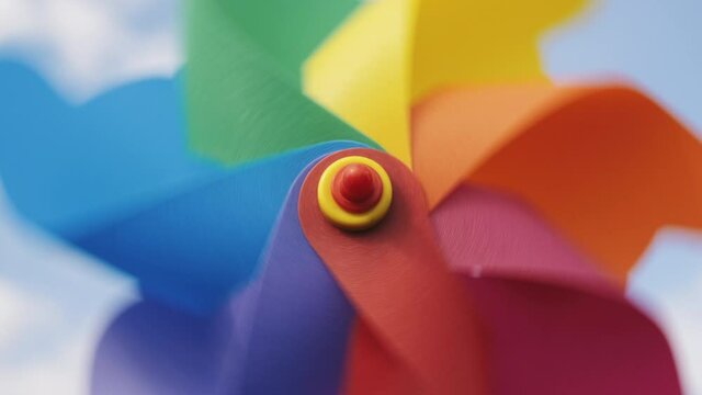 Pinwheel rotating colored spinning plastic with blowing wind against blue sky and white clouds summer sunny day slow motion. Symbol of freedom and childhood. Toy spinner.  Relax