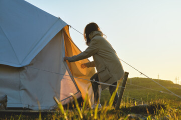 young girl opens a glamping tent in the middle of a green field in the sunset rays. Camping and outdoor concept.