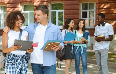 Smiling student cuddling his black girlfriend outdoors during break in classes